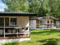 Dwa białe domki kempingowe w lesie, z werandami i meblami ogrodowymi. Idealne miejsce dla każdego **camping wagabunda**.