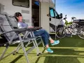Kobieta odpoczywa na leżaku obok kampera na dziko, z rowerami w tle.