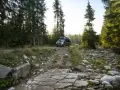 Kamper w górskiej scenerii Szwajcarii, na kamienistej drodze wśród świerków.