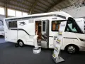 Biała kamperka z otwartymi drzwiami na targach caravaningowych Poznań. W środku widać wyposażenie, a na zewnątrz stojaki z ulotkami.