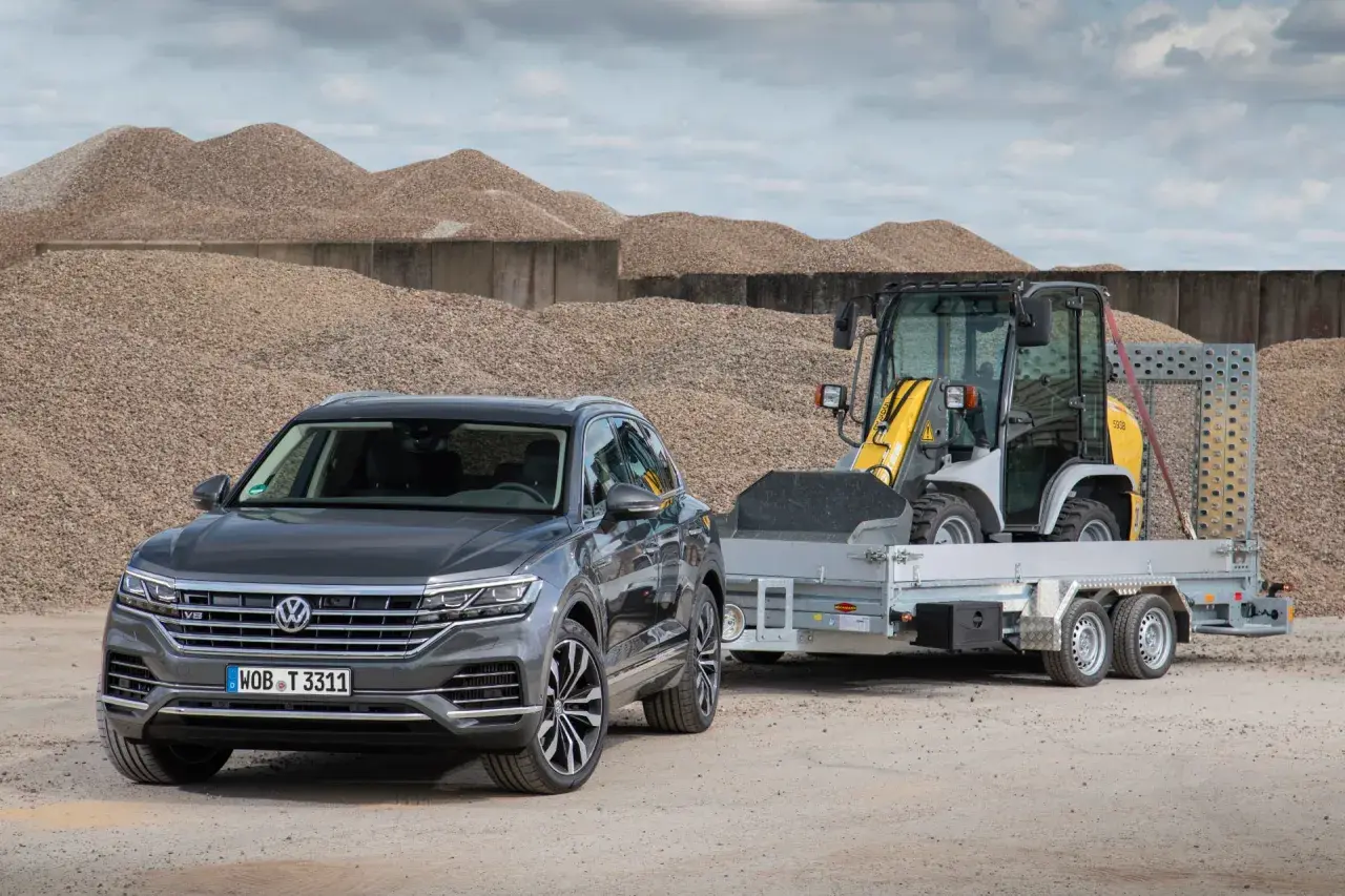 Szary Volkswagen Touareg z przyczepą, na której stoi ładowarka. To auto ma 3,5 tony na haku, gotowe do pracy.