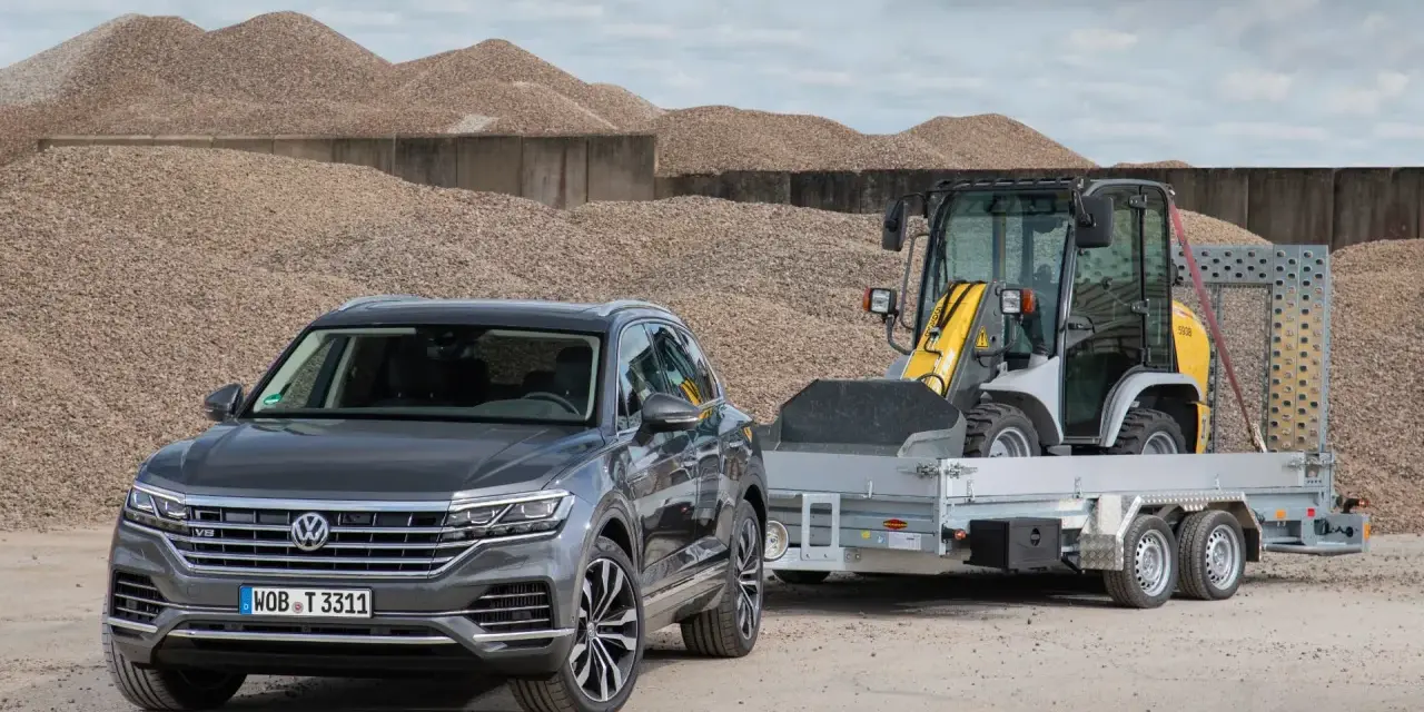 Szary Volkswagen Touareg z przyczepą, na której stoi ładowarka. To auto ma 3,5 tony na haku, gotowe do pracy.