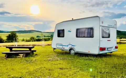 Przyczepa Caravelair zaparkowana na łące o zachodzie słońca. W tle malownicze wzgórza i pola.