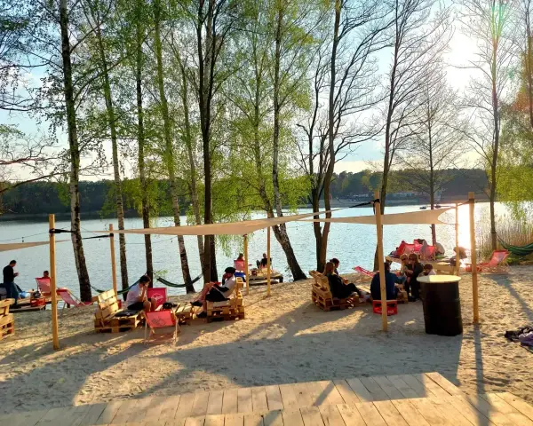 Relaks na plaży nad jeziorem, idealne miejsce na camping Polska. Ludzie odpoczywają na leżakach i paletach pod namiotami.