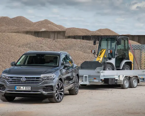 Szary Volkswagen Touareg z przyczepą, na której stoi ładowarka. To auto ma 3,5 tony na haku, gotowe do pracy.