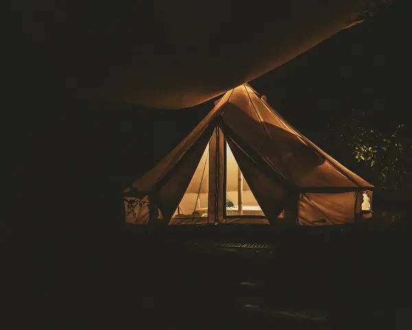 Nocą oświetlony namiot na darmowych miejscach biwakowych. Ciepłe światło wydobywa się z wnętrza, tworząc przytulną atmosferę.