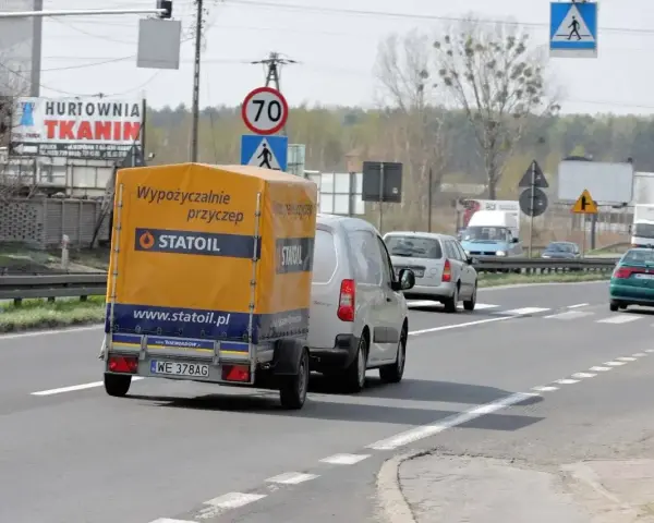 Samochód z żółtą przyczepką Statoil jedzie drogą. Znak ograniczenia do 70 km/h sugeruje, ile można jechać z przyczepką w tym miejscu.