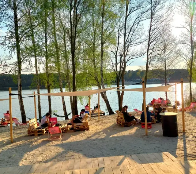 Relaks na plaży nad jeziorem, idealne miejsce na camping Polska. Ludzie odpoczywają na leżakach i paletach pod namiotami.