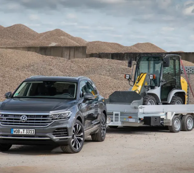 Szary Volkswagen Touareg z przyczepą, na której stoi ładowarka. To auto ma 3,5 tony na haku, gotowe do pracy.