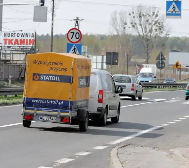 Samochód z żółtą przyczepką Statoil jedzie drogą. Znak ograniczenia do 70 km/h sugeruje, ile można jechać z przyczepką w tym miejscu.
