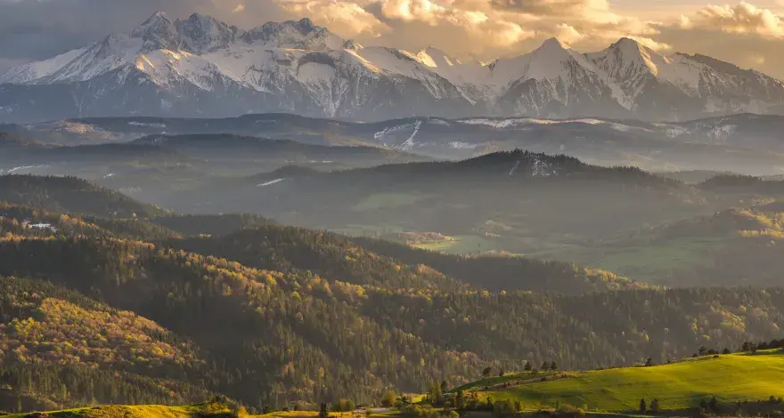Złote światło oświetla najpiękniejsze szczyty w Polsce, Tatry, otoczone przez malownicze, zalesione wzgórza.