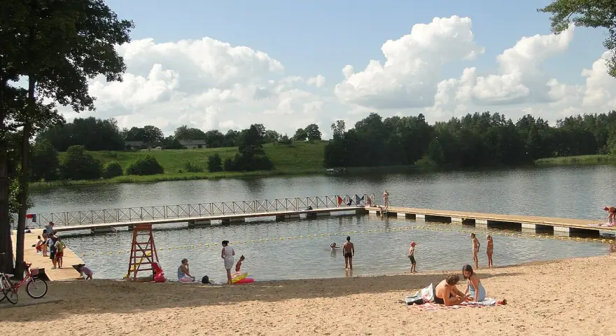 Słoneczne plaże na Mazurach tętnią życiem. Ludzie odpoczywają na piasku, kąpią się w jeziorze i spacerują po pomoście.