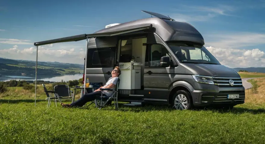 Mężczyzna odpoczywa przy kamperze VW California. Wymiary tego pojazdu pozwalają na komfortowe podróżowanie i biwakowanie.