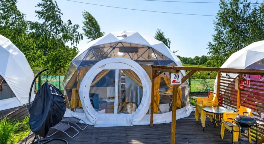 Nowoczesne namioty sferyczne na energylandia pole namiotowe. Drewniany taras z grillem i żółtymi krzesłami.