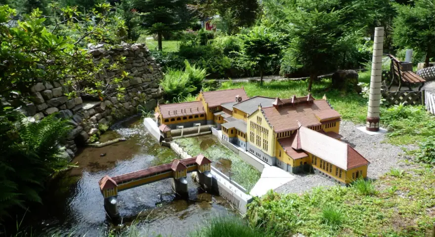 Miniaturowa zabudowa z mostkiem i budynkami, jak w parkach miniatur w Polsce.