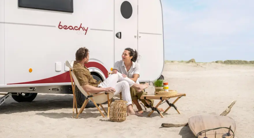 Para na plaży przy kamperze, relaksująca rozmowa. To właśnie karawaning co to – wolność i przygoda.