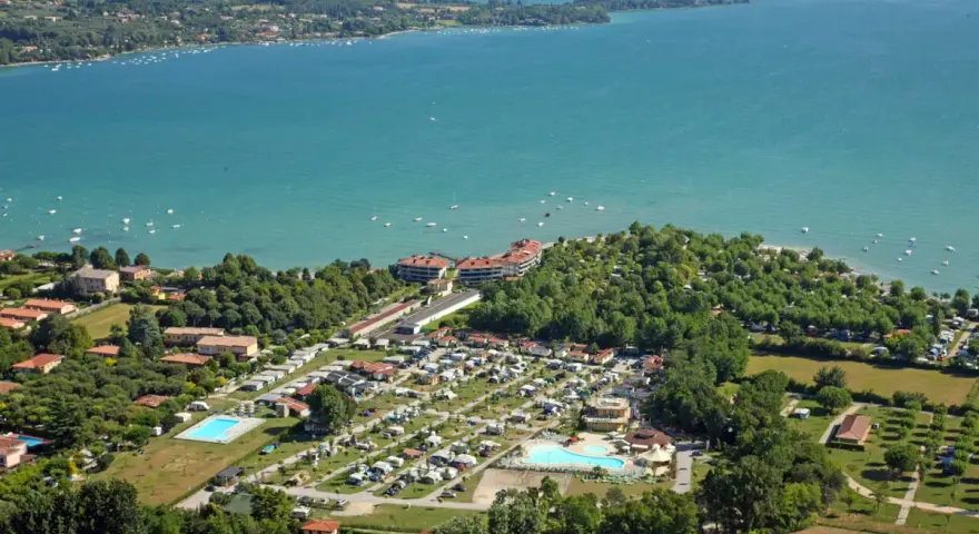 Widok z lotu ptaka na camping Baia Verde nad turkusowym jeziorem, z basenami i licznymi namiotami.