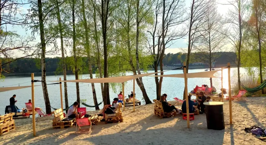 Relaks na plaży nad jeziorem, idealne miejsce na camping Polska. Ludzie odpoczywają na leżakach i paletach pod namiotami.
