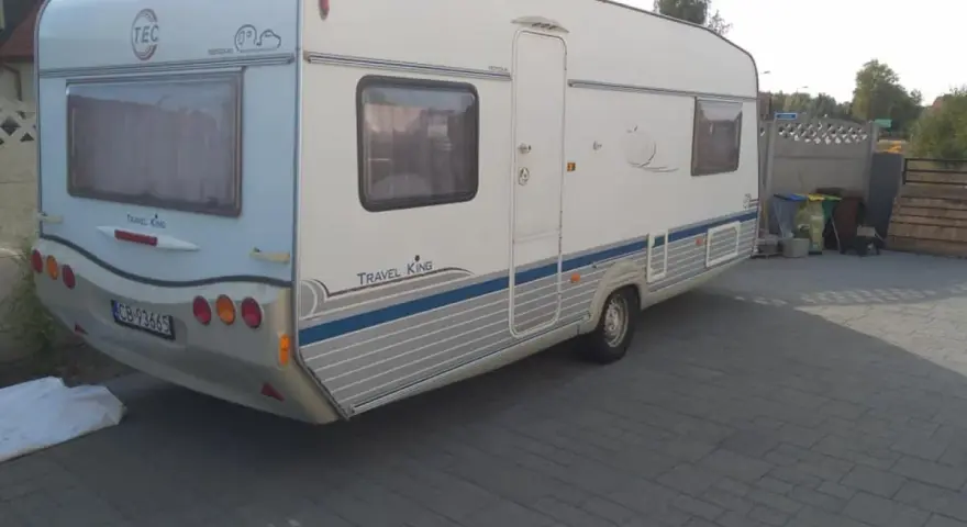 Biała przyczepa kempingowa TEC Travel King z niebieskimi pasami, gotowa na wakacyjne podróże.
