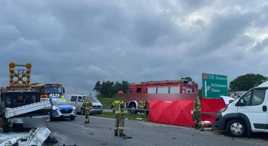 Miejsce wypadku kampera. Straż pożarna i policja zabezpieczają teren po zdarzeniu drogowym. Widoczny rozbity pojazd i czerwony namiot.
