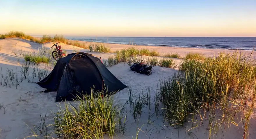 Namiot i rower na plaży, idealne miejsce na biwakowanie na dziko. Wschód słońca nad morzem.