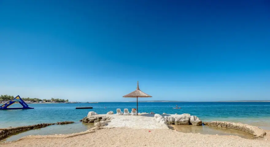 Słoneczny dzień na plaży w Simuni camping. Leżaki pod parasolem, dmuchany plac zabaw w wodzie i błękitne morze.