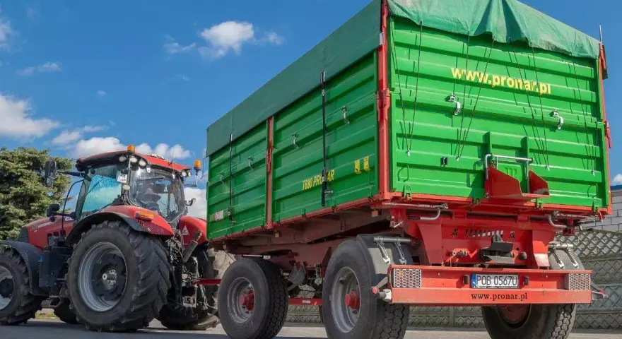 Czerwony traktor z zieloną przyczepą. Dowiedz się, jakich przyczep nie trzeba rejestrować, by ułatwić sobie pracę w gospodarstwie.