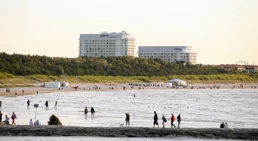 Ludzie spacerują po najszerszej plaży w Polsce, w tle hotele Radisson i Hilton.