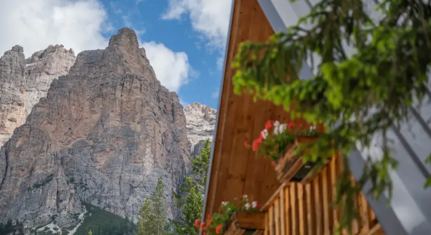 Drewniany domek z kwiatami w skrzynkach na tle skalistych Dolomitów.