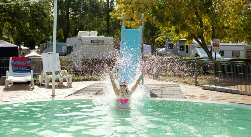Radość na aranypart camping! Dziecko zjeżdża ze zjeżdżalni prosto do basenu, tworząc fontannę wody.
