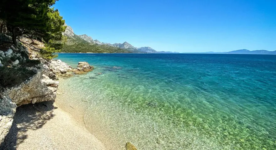 Idealne miejsce na camping w Chorwacji: kamienista plaża, turkusowa woda i góry w tle.
