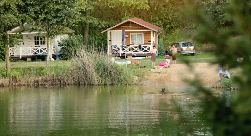 Rodzina odpoczywa nad jeziorem w malowniczym miejscu. Dzieci pluskają się w wodzie, a dorośli relaksują się na plaży przy domkach kempingowych. To idealne miejsce na rodzinne wakacje, prawdziwa **camping forteca** spokoju i radości.