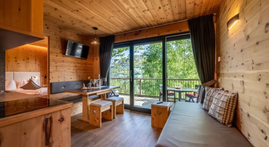 Przytulny domek z widokiem na góry, idealny na camping Seiser Alm. Drewniane wnętrze, wygodna kanapa i stół zapraszają do relaksu.