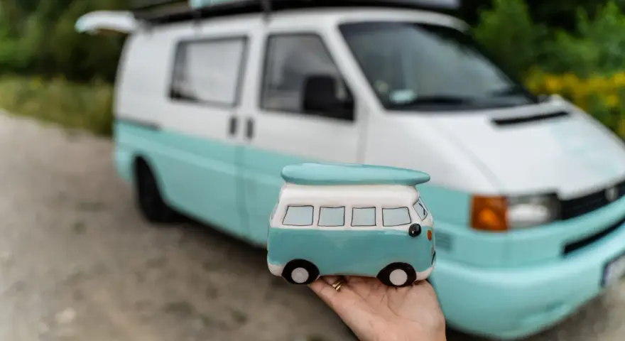 Mała figurka t4 camper w ręce, na tle prawdziwego, turkusowo-białego kampera.