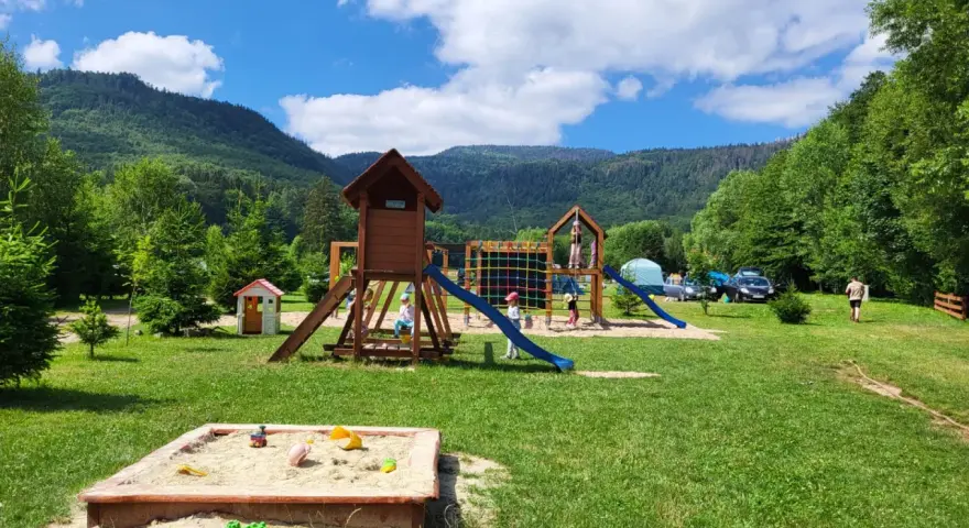 Plac zabaw dla dzieci na terenie radków camping. Piaskownica, zjeżdżalnie i drabinki w otoczeniu zieleni i gór.