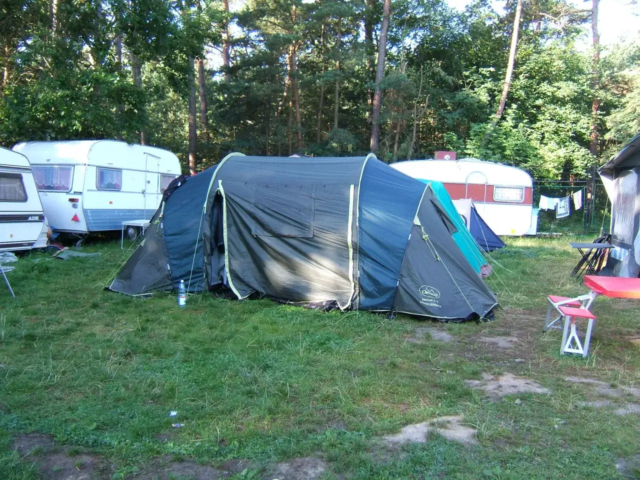 Caravaning w Juracie: duży namiot i przyczepy kempingowe na trawiastym polu wśród drzew.