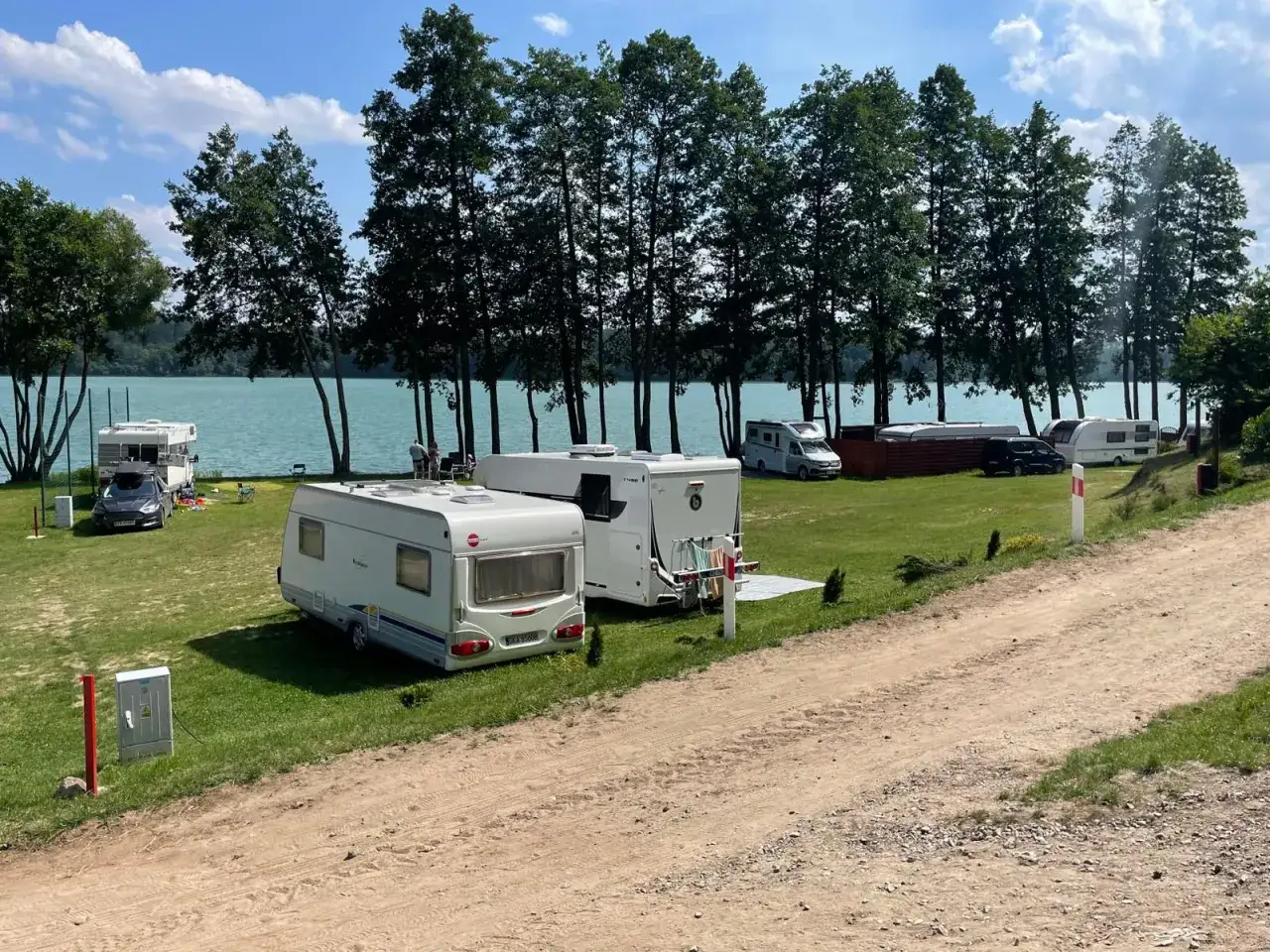 Malownicze kempingi w Polsce nad jeziorem. Przyczepy kempingowe i kampery na zielonej trawie, w tle las i błękitna woda.