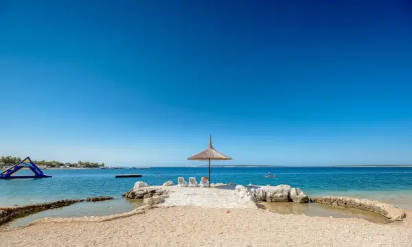 Słoneczny dzień na plaży w Simuni camping. Leżaki pod parasolem, dmuchany plac zabaw w wodzie i błękitne morze.