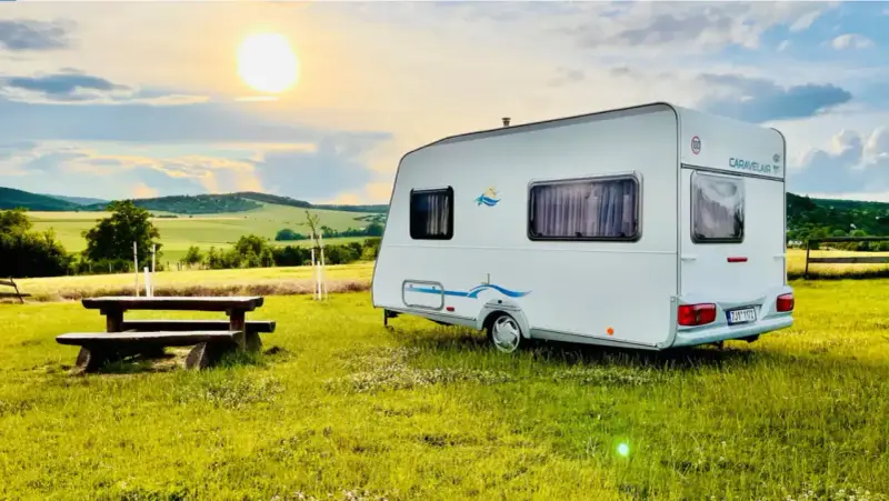 Przyczepa Caravelair zaparkowana na łące o zachodzie słońca. W tle malownicze wzgórza i pola.
