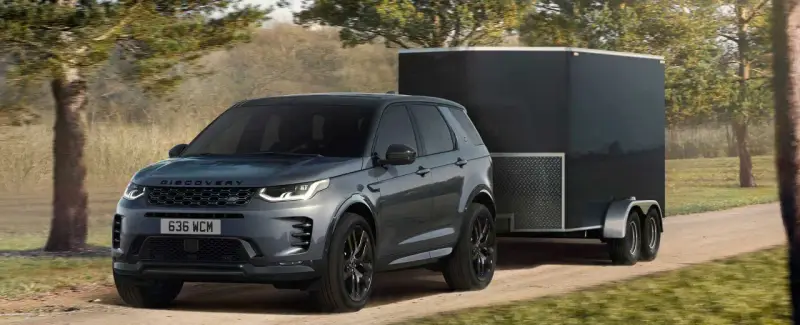 Szary Land Rover Discovery Sport z przyczepą o masie 2000 kg jedzie po leśnej drodze.