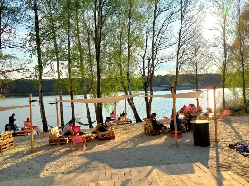 Relaks na plaży nad jeziorem, idealne miejsce na camping Polska. Ludzie odpoczywają na leżakach i paletach pod namiotami.