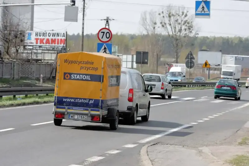 Samochód z żółtą przyczepką Statoil jedzie drogą. Znak ograniczenia do 70 km/h sugeruje, ile można jechać z przyczepką w tym miejscu.